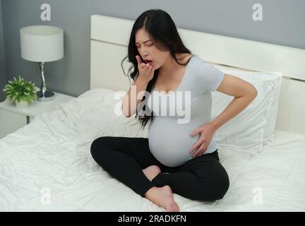sick pregnant woman feeling unwell and coughing on a bed Stock Photo