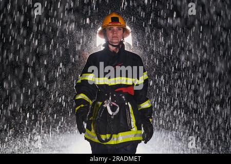 A determined female firefighter in a professional uniform striding through the dangerous, rainy night on a daring rescue mission, showcasing her Stock Photo