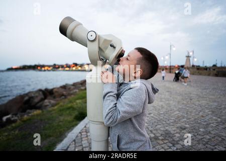 Boy looks at the sea through a coin operated telescope in the evening Nessebar. Stock Photo