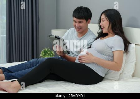 pregnant woman with her husband using digital tablet on a bed Stock Photo
