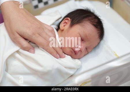 hand of mother putting her newborn baby to sleep in the infant bassinet basket at hospital Stock Photo