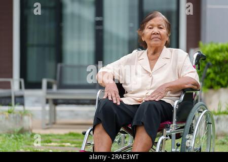 senior woman sitting in wheelchair at outside the house Stock Photo