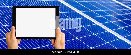 Digital tablet with blank screen in hands on background of blue solar panel. Stock Photo