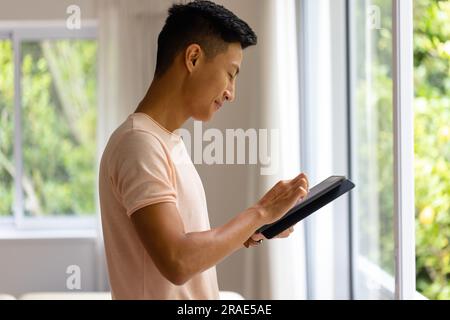 Profile of happy asian man using tablet in bright room Stock Photo