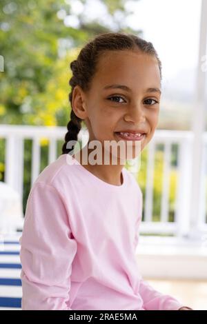 Portrait of happy biracial girl wearing pyjamas in bedroom in front of window with view of garden Stock Photo