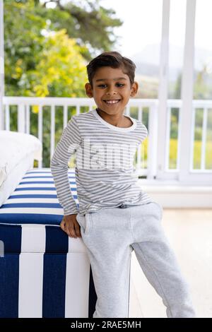 Portrait of happy biracial boy wearing pyjamas in bedroom in front of window with view of treetops Stock Photo