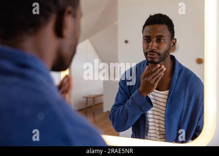 Happy african american man in bathrobe looking in mirror in bathroom Stock Photo
