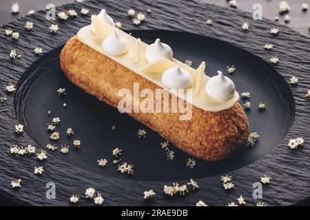French eclair grazed with chocolate or sweet Italian profiteroles on a black stone plate, gourmet confectionery food Stock Photo