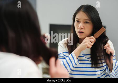 unhappy woman is having problems with combing hair tangled in mirror at home Stock Photo