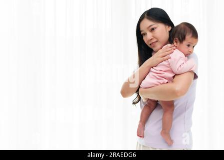 mother holding newborn baby burping after feeding milk on white window background Stock Photo