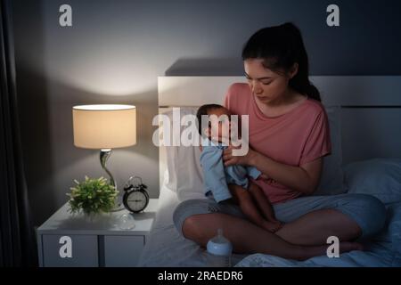 mother holding newborn baby burping after feeding milk on a bed at night Stock Photo