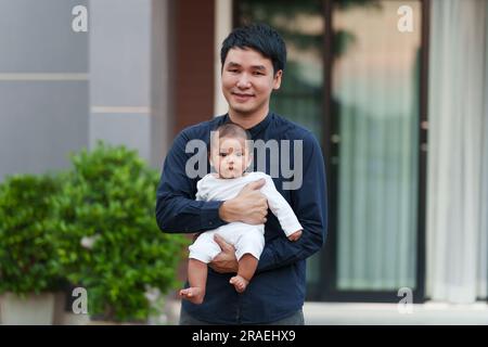 happy father holding with newborn baby while standing in front of their house Stock Photo
