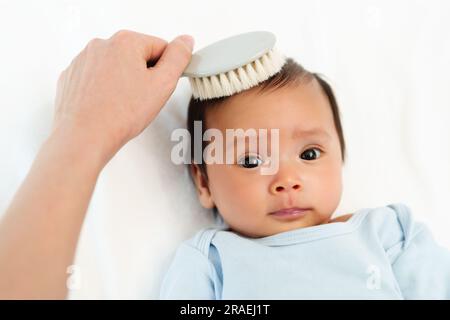 mother combing her newborn baby hair on a bed Stock Photo
