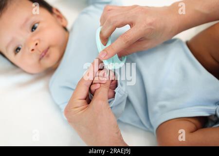 mother cutting newborn baby's hand fingernails with nail scissors. Stock Photo