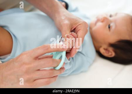 mother cutting newborn baby's hand fingernails with nail scissors. Stock Photo