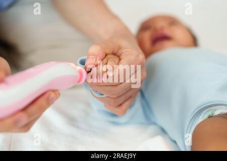 mother cutting newborn baby's fingernails with auto electic nail trimmer. Stock Photo