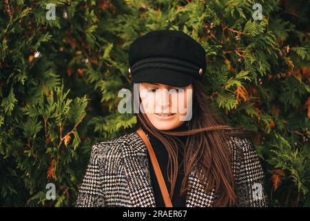 Outdoor portrait of beautiful young woman with dark hair, wearing check blazer and black cap Stock Photo