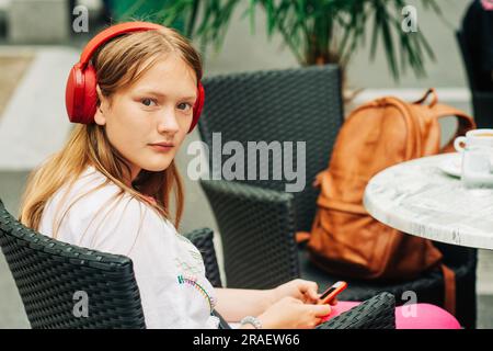 Young preteen girl resting in cafe, wearing earphones, backpack on the chair Stock Photo