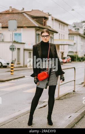 Outdoor fashion portrait of young stylish woman posing on the street by the road, wearing black jacket, check skirt Stock Photo