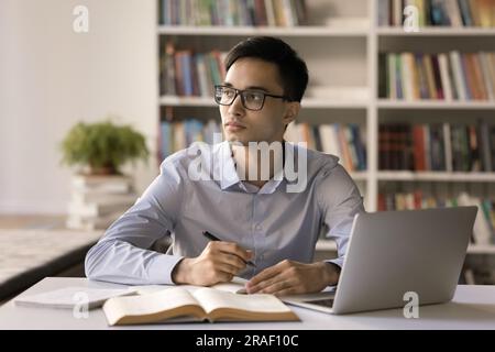 Pensive smart student guy in glasses studying in university library Stock Photo