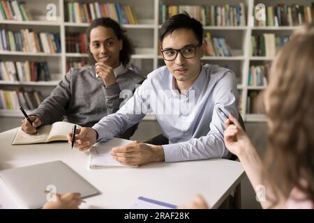 Positive diverse high school students sitting at table in library Stock Photo