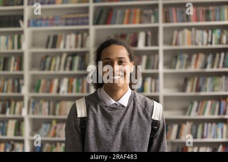 Cheerful African American student guy with backpack standing in library Stock Photo