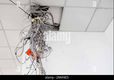 Electrical wires hanging from the ceiling. Cables hanging from ceiling of room. Building under construction. Work in progress. Stock Photo