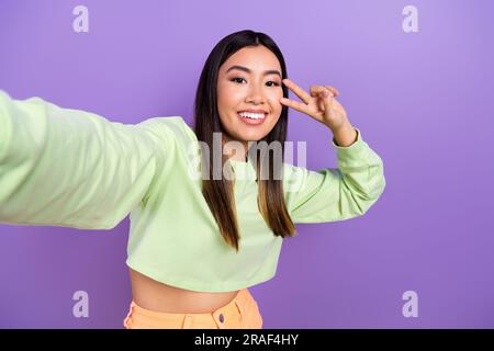 Photo of positive pretty woman with dyed hairdo dressed green clothes making selfie show v-sign isolated on purple color background Stock Photo