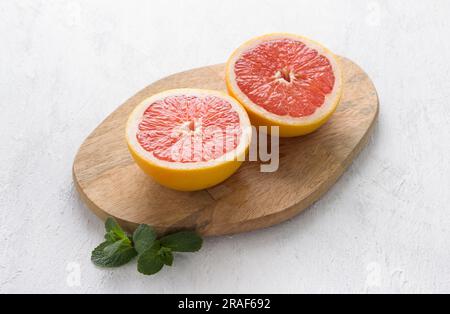 Wooden board with two halves of a grapefruit on a light gray background, top view. Stock Photo