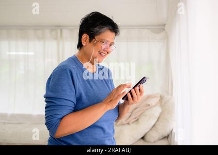 Healthy mature woman holding smartphone using mobile app and chatting with friends, Senior people with technology at home, Grandmother relaxing at Stock Photo