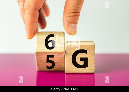 time for the 6G symbol. The hand rotates the wooden cube and changes the 5G sign to 6G. Concept, technology development, high speed communication netw Stock Photo
