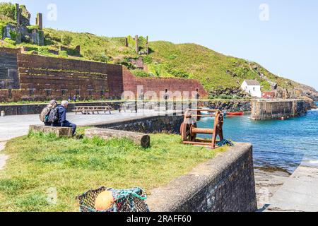 A couple of walkers on the Pembrokeshire Coast Path National Trail taking a breather at Porthgain harbour, Pembrokeshire, Wales UK Stock Photo