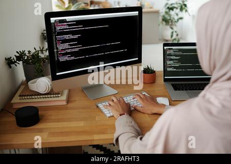 Hands of young Muslim female IT engineer typing on computer keyboard while sitting by workplace in front of screen and decoding data Stock Photo