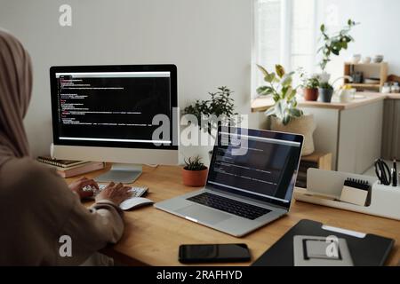 Young Muslim woman in headscarf decoding data or developing new software while typing on computer keyboard by workplace in home office Stock Photo