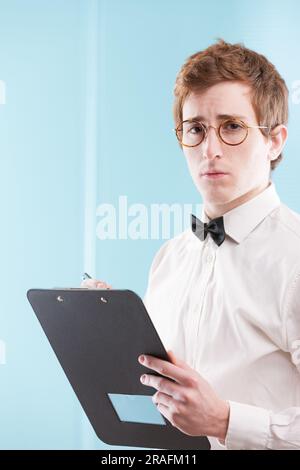 A young man in an old-fashioned office suit, possibly a nerdy, slightly servile accountant, grips a notepad. His sad gaze, white shirt, and bowtie sta Stock Photo