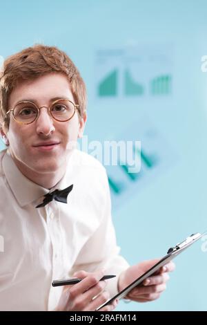 In focus, a young man with a nerdy, subservient vibe, wears a dated office suit and holds a notepad. His white shirt, bowtie, and sad gaze hint at an Stock Photo