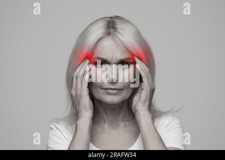 Migraine Concept. Mature woman with headache touching red sore zones on temples Stock Photo