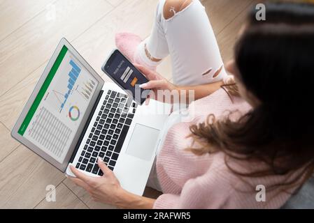 Female using mobile banking on smart phone, analysis on laptop Stock Photo