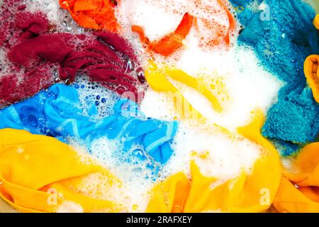 Colored clothes soaked in water with detergent and foam bubbles. Washing by hand. Stock Photo