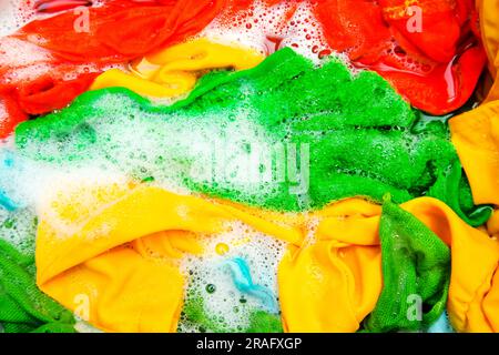 Colored clothes soaked in water with detergent and foam bubbles. Washing by hand. Stock Photo