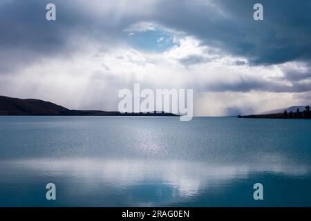 Photograph of early morning sun shining through rain clouds on Lake Tekapo on the South Island of New Zealand Stock Photo