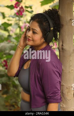 Old woman jogging in the park on a Jogging track and trail taking care of her health. She is listening to music using headphones on a jogging break Stock Photo