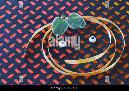 Text space on abstract geometric pattern background is highlighted with ribbon face, eyes, leaves. See happy pumpkin round against orange & red colors. Stock Photo