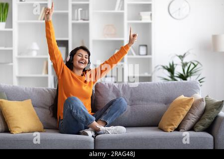 Positive millennial eastern lady enjoying music at home Stock Photo