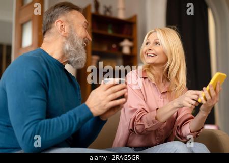 Senior Man And Woman Using Smartphone Drinking Coffee At Home Stock Photo