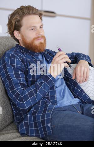 young man on sofa using vaporizer as smoking alternative Stock Photo