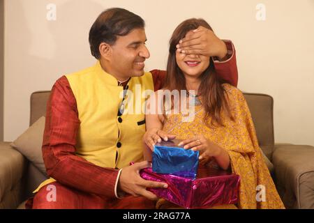 Happy Indian man brings Surprise gift for his Indian wife in saree. Both are wearing Indian ethnic clothes on Diwali festival. Stock Photo