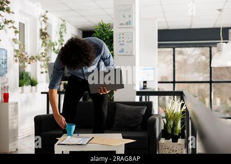 Arab young businessperson holding laptop in start up business office. Entrepreneur putting coffee mug on table to work at company marketing strategy plan on computer after break Stock Photo