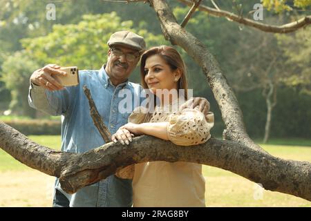 Aged Indian couple having a good romantic time in the green park. They are enjoying, smiling and having joyful moments. Stock Photo