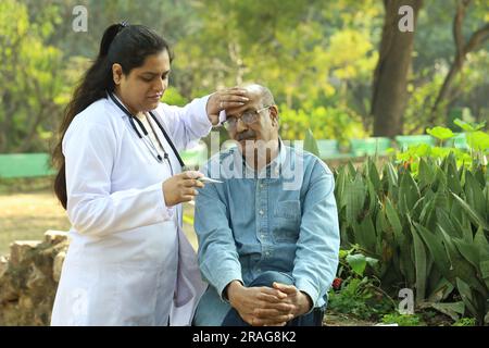 Female Indian doctor examining the senior patient in the city park in afternoon. Stock Photo